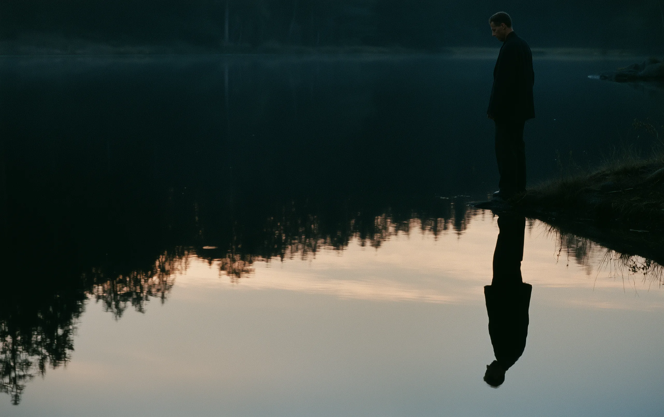A man stands upright at the edge of a completely still lake, looking down at his own reflection, and as you watch, the reflection stops matching him: it stands bowed, its head lowered